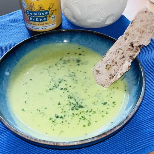 Cremige Zucchinicremesuppe in einer blauen Schüssel mit frischen Kräutern und glutenfreiem Brot, histaminarm serviert.