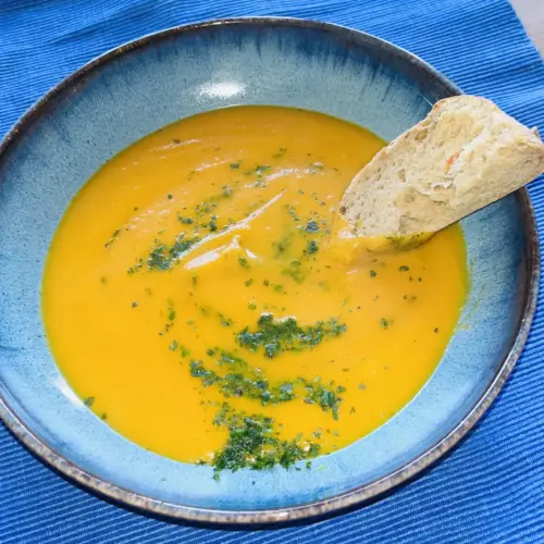 Cremige Karottencremesuppe mit Kokosmilch, garniert mit Kräutern, serviert in einer blauen Schüssel mit Brot