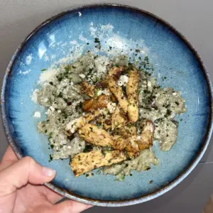 Zucchini-Nockerln aus Buchweizenmehl mit gebratenem Hähnchen und Zucchini-Basilikum-Pesto in einer blauen Schüssel.